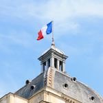 The French flag waves atop the dome of historic architecture in Paris, France.
