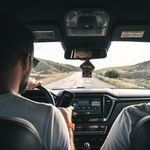 How to Choose Your First US Road Trip Route 1 Two men driving through a scenic landscape, using a cellphone for navigation.