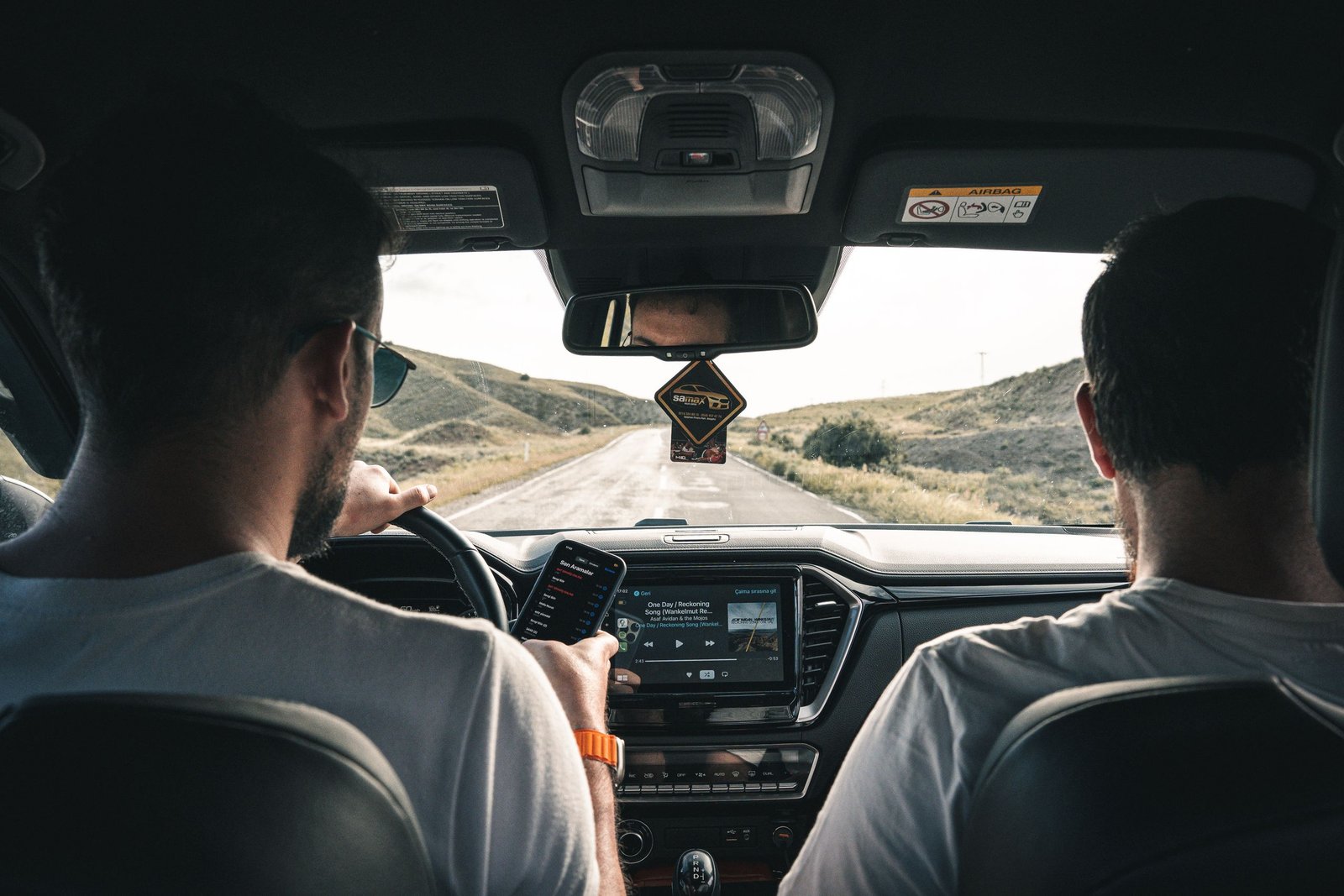 How to Choose Your First US Road Trip Route 1 Two men driving through a scenic landscape, using a cellphone for navigation.